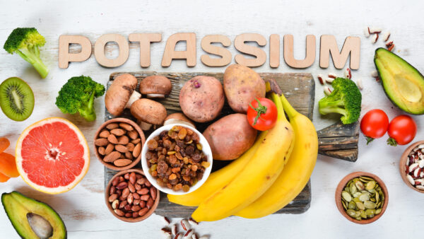 Foods containing natural potassium. K: Potatoes, mushrooms, banana, tomatoes, nuts, beans, broccoli, avocados. Top view. On a white wooden background.