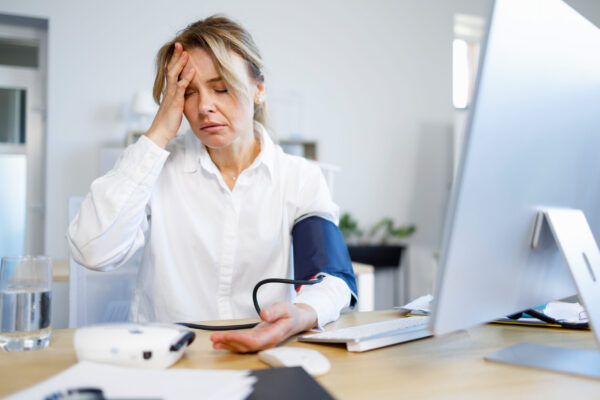 Exhausted business woman measuring her blood pressure and pulse at workplace