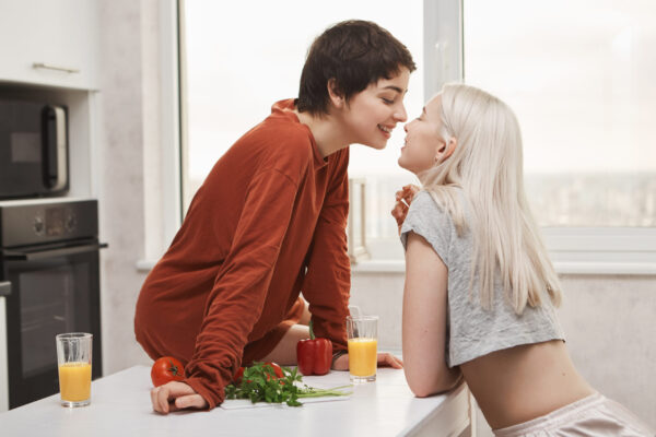 LGBTQ sexual wellness through nutrition - stylish-attractive-lesbian-red-pullover-sitting-kitchen-table-while-kissing-girlfriend-smiling-happily-during-breakfast-girl-finally-found-her-soulmate-scaled